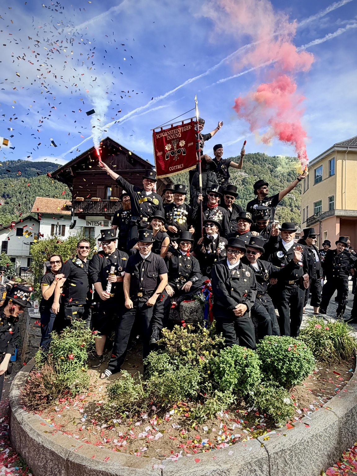 Eine Gruppe von Schornsteinfegern feiert mit Fahne, Konfetti und farbigem Rauch.