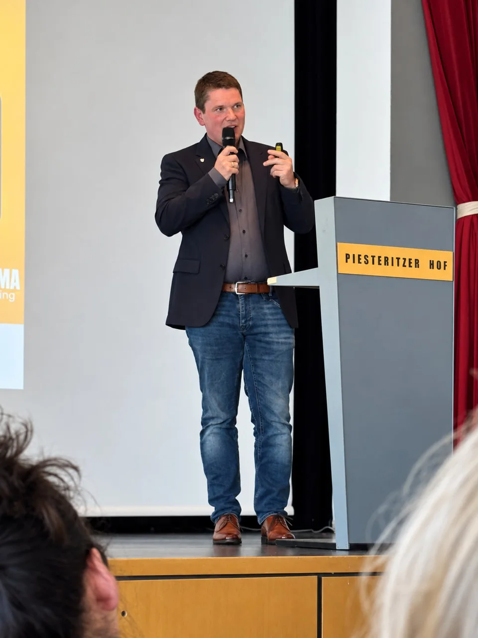 Rainer Schamberger mit Mikrofon und Presenter auf der Bühne im Piesteritzer Hof